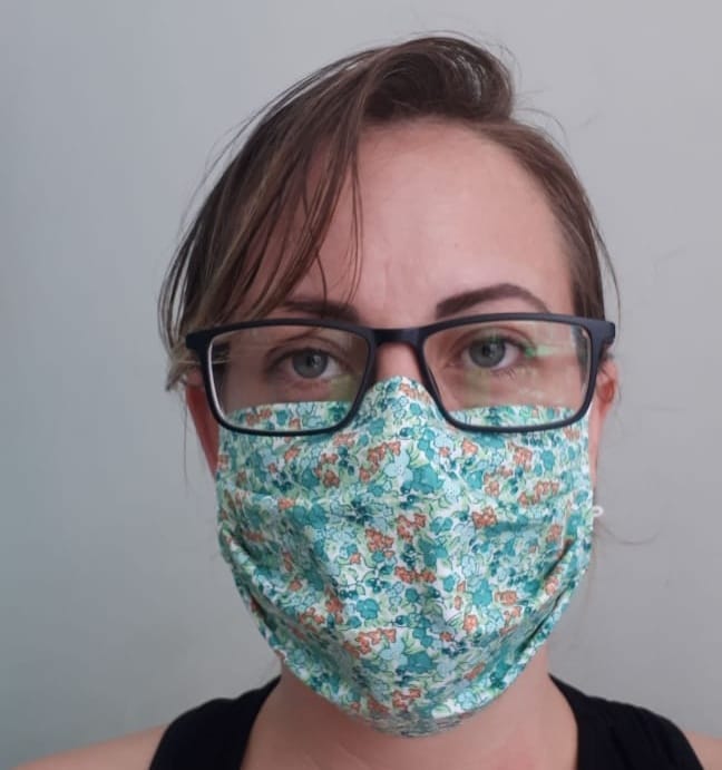 A foto mostra uma mulher jovem usando uma máscara de tecido produzida pela família. 